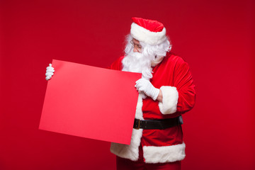 Naklejka premium Santa Claus pointing in blank advertisement banner isolated on red background with copy space red leaf
