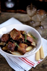 Baked beef ribs with potatoes and thyme on an old wooden background.