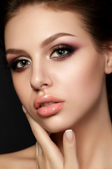 Fototapeta na wymiar Portrait of young beautiful woman with evening make up touching her face over black background. Multicolored smokey eyes. Luxury skincare and modern fashion makeup concept. Studio shot.
