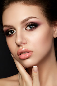 Portrait of young beautiful woman with evening make up touching her face over black background. Multicolored smokey eyes. Luxury skincare and modern fashion makeup concept. Studio shot.