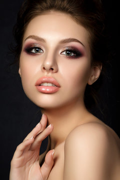 Portrait of young beautiful woman with evening make up touching her face over black background. Multicolored smokey eyes. Luxury skincare and modern fashion makeup concept. Studio shot.