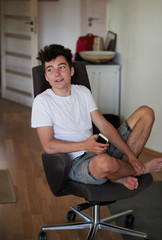 Fototapeta premium Boy holding smartphone sitting in chair at home