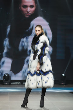 Beautiful fashion model  walks on runway in fur coat with online screen on background