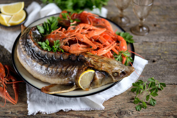 Baked whole sturgeon with boiled crawfish and lemon on an old wooden background. Rustic style.