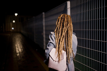 Girl with dreadlocks walking at night street of city.