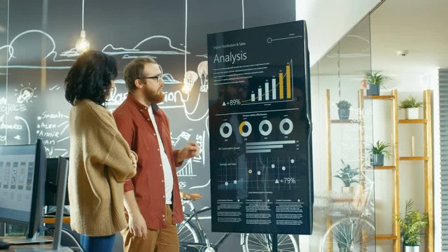 Female Developer and Male Statistician Use Interactive Whiteboard Presentation Screen to Look at Charts, Graphs and Growth Statistics.  Shot on RED EPIC-W 8K Helium Cinema Camera.