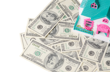 Mortgage or real estate concept. Small house standing on the plenty of one hundred dollar bills isolated on a white.