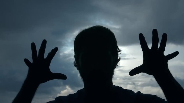 Silhouette of a creepy man with twitching hands and fingers comes at camera attacking with transition to black.