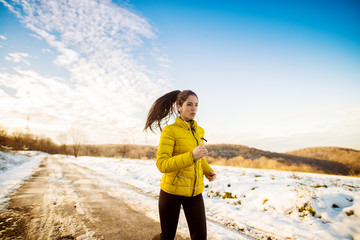 Young persistent fitness focused girl running in winter sportswear outside in nature.