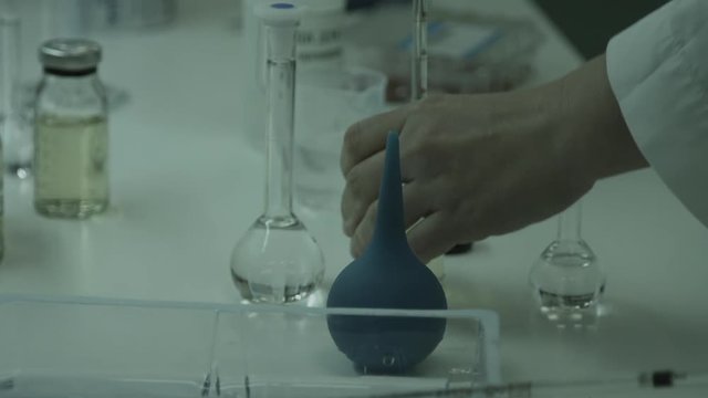 The employee works in laboratory of the pharmaceutical plant. Close up. Table and manipulations with reactants with hands is visible in a shot. Without color correction.