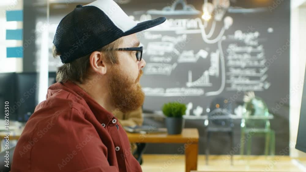 Poster in the creative agency videographer in a cap works on personal computer with two monitors, he's doin