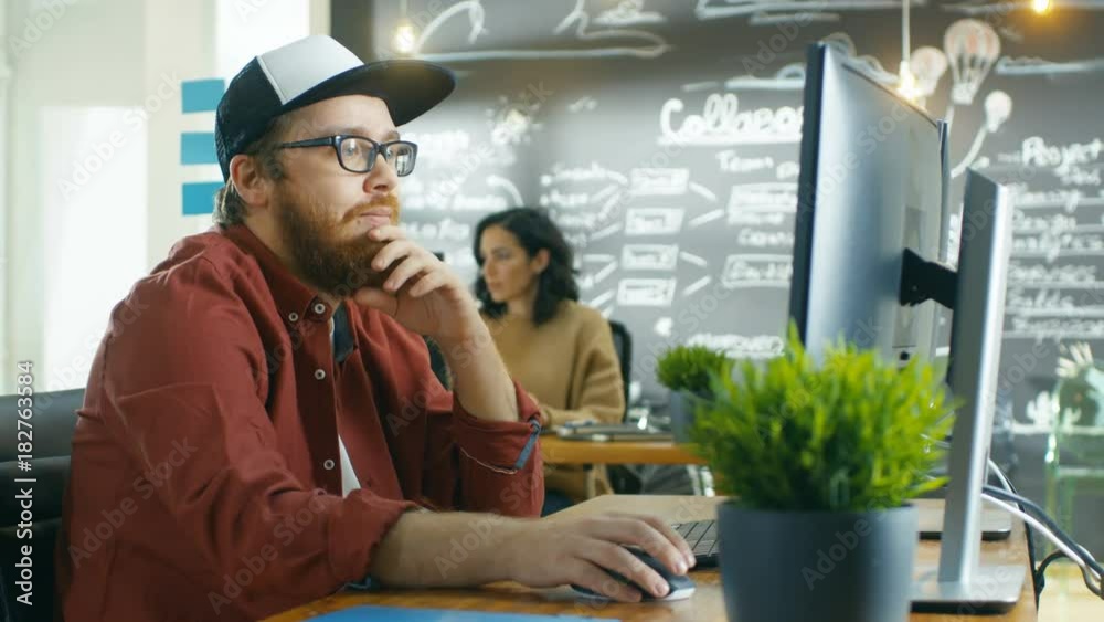 Poster in the creative agency videographer in a cap works on personal computer with two monitors, he's doin