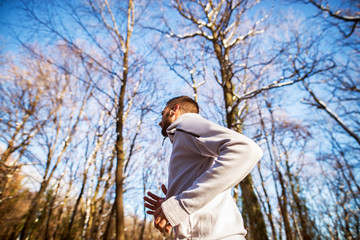 Rear view of young runner man in sportswear jogging in the sunny winter morning outside in nature.