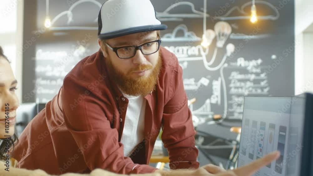 Poster Beautiful Woman Developer Uses Personal Computer and Talks With a Bearded Programer in a Cap, Together They Design New Mobile Video Game/ Application. Shot on RED EPIC-W 8K Helium Cinema Camera.