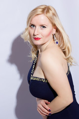 Studio portrait of a beautiful young blond woman in a blue evening dress and long diamond earrings.