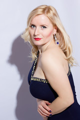 Fototapeta premium Studio portrait of a beautiful young blond woman in a blue evening dress and long diamond earrings.