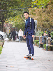 Fototapeta premium Portrait of handsome Chinese young man go to work with a skateboard.