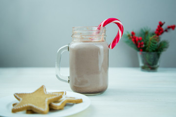A glass jar of cocoa with Christmas star ginger cookies and a red candy cane