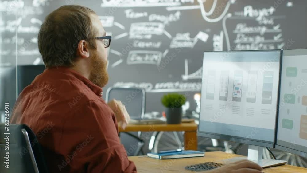 Aufkleber Male Mobile Video Game Application Developer Works on a Personal Computer, Designing Wireframe, He's Smooths the Beard in Thinking Gesture. Shot on RED EPIC-W 8K Helium Cinema Camera.