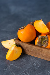 Persimmon fruit in a wooden box on a dark background. Cut fruit.