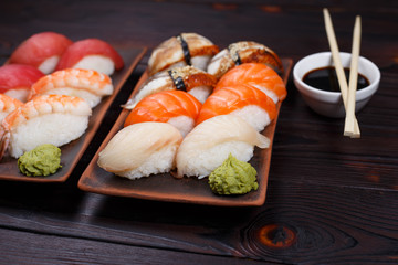 Delicious appetizing nigiri sushi, served on clay plates with soy sauce and chopsticks on dark wooden table. Traditional Japanese food, tasty seafood, sushi restaurant concept