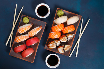 Delicious appetizing nigiri sushi set, served on clay plates with soy sauce and chopsticks, flat lay on dark green table. Traditional Japanese food, tasty seafood, sushi restaurant concept