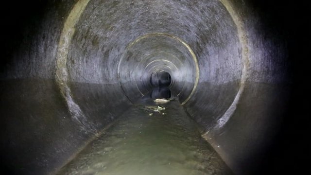 Dark underground sewer round concrete tunnel. Industrial wastewater and urban sewage flowing throw sewer pipe