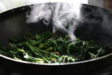 Stir-Fried Chinese Morning Glory hot cooking with smoke on fire in Thai kitchen