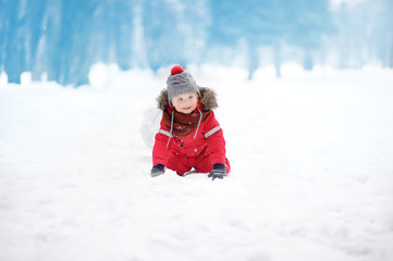Fototapeta na wymiar Little boy in red winter clothes having fun with snowball