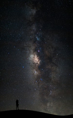 silhouette of a standing photographer on the mountain and colorful milky way galaxy with space dust and stars in the space, long exposure with grain.