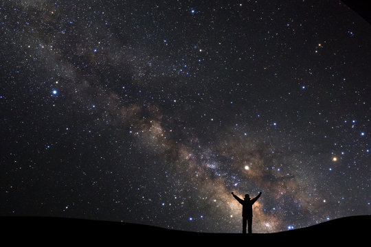 landscape with milky way, Night sky with stars and silhouette of a standing sporty man with raised up arms on high mountain.