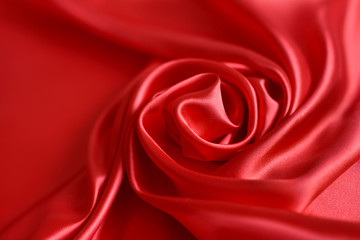 Close up of ripplesin shape of rose flower in red silk fabric. Satin textile background.