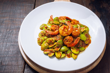 Thai food on white plate and wooden table, Spicy stir-fried shrimp with bitter or twisted cluster or stink bean ( sataw ) and shrimp paste