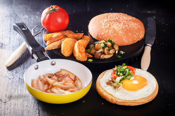 Breakfast with fried egg on bread, bacon, mushrooms, tomatoes and greens. Black background