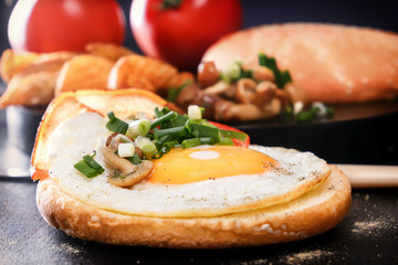 Breakfast. Fried egg on a roll, tomato, greens, bacon, mushrooms. Cutlery. Close-up Black background