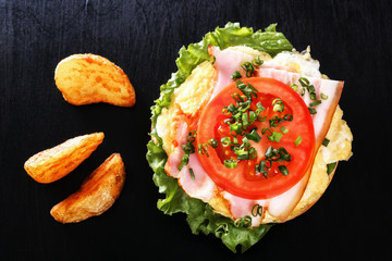 Sandwich with fried egg, bacon, tomato, greens. Breakfast with fried potatoes and mushrooms. Top view. Black background