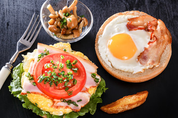 Fried egg on a roll. Sandwich with bacon, tomato and vegetables. Mushrooms. Breakfast. Black background