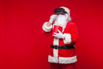 Santa Claus wearing virtual reality goggles and a red bucket with popcorn, on a red background. Christmas