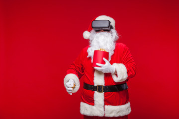 Santa Claus wearing virtual reality goggles and a red bucket with popcorn, on a red background. Christmas