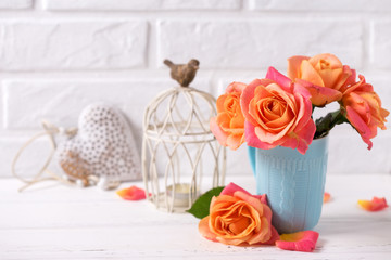 Fresh orange roses in blue cup, heart ans candle  on white wooden background