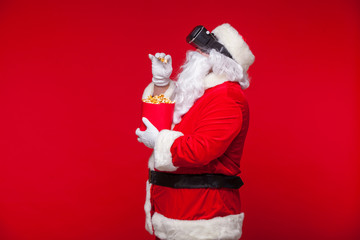 Santa Claus wearing virtual reality goggles and a red bucket with popcorn, on a red background. Christmas