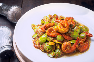Thai food on white plate and wooden table, Spicy stir-fried shrimp with bitter or twisted cluster or stink bean ( sataw ) and shrimp paste