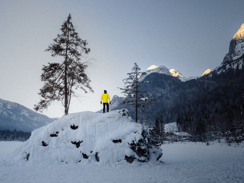 Mann mit gelber Jacke bewundert den Sonnenaufang in winterlicher schneebedeckter Landschaft mit Bergen