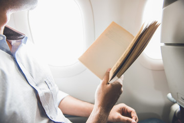 Male passenger killing time by reading book while traveling on the airplane
