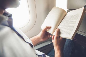 Male passenger killing time by reading book while traveling on the airplane