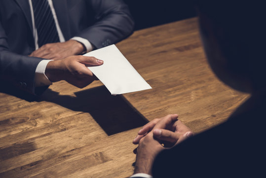 Businessman giving money in the envelope to his partner in the dark