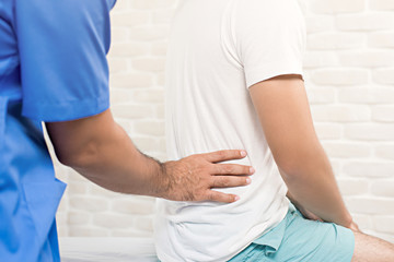 Male doctor therapist treating lower back pain patient in clinic