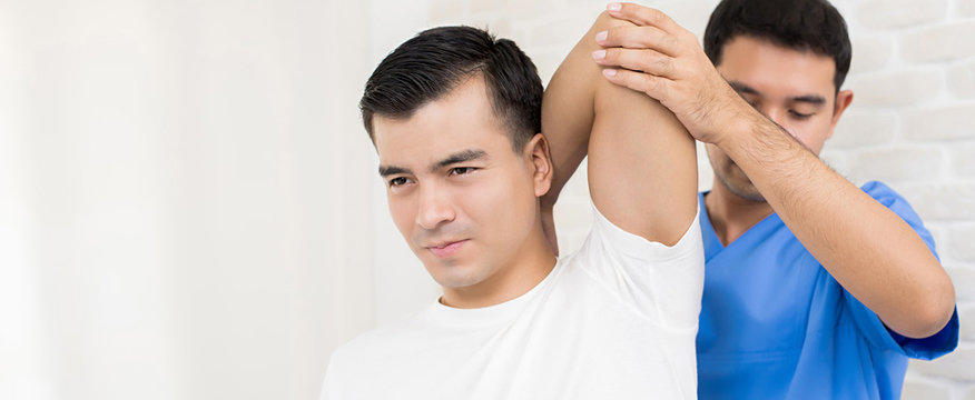 Therapist training rehab exercise, overhead tricep stretching, to male patient in hospital