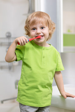 Happy kid or child brushing teeth in bathroom. Dental hygiene.