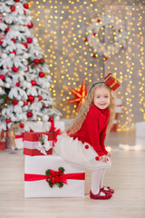 Young beautiful girl smiling, sitting near huge golden mirror plenty presents on fur Christmas green white luxury tree decorations and beneath lie gifts